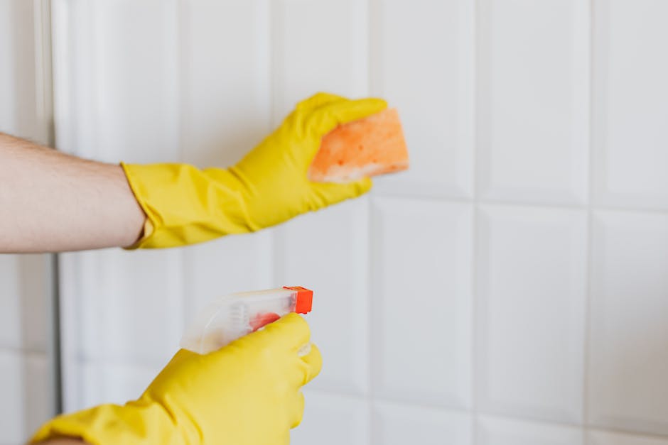 A person wearing brown cleaning gloves is adjusting a lightbox sign displaying the words 'CLEANING HOME' in black letters on illuminated white background panels, set on a wooden table in a modern livi